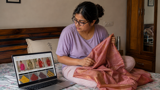 Indian woman sitting on a bed, comparing pink silk fabric while browsing FabricRoot fabrics on a laptop in a cozy bedroom.