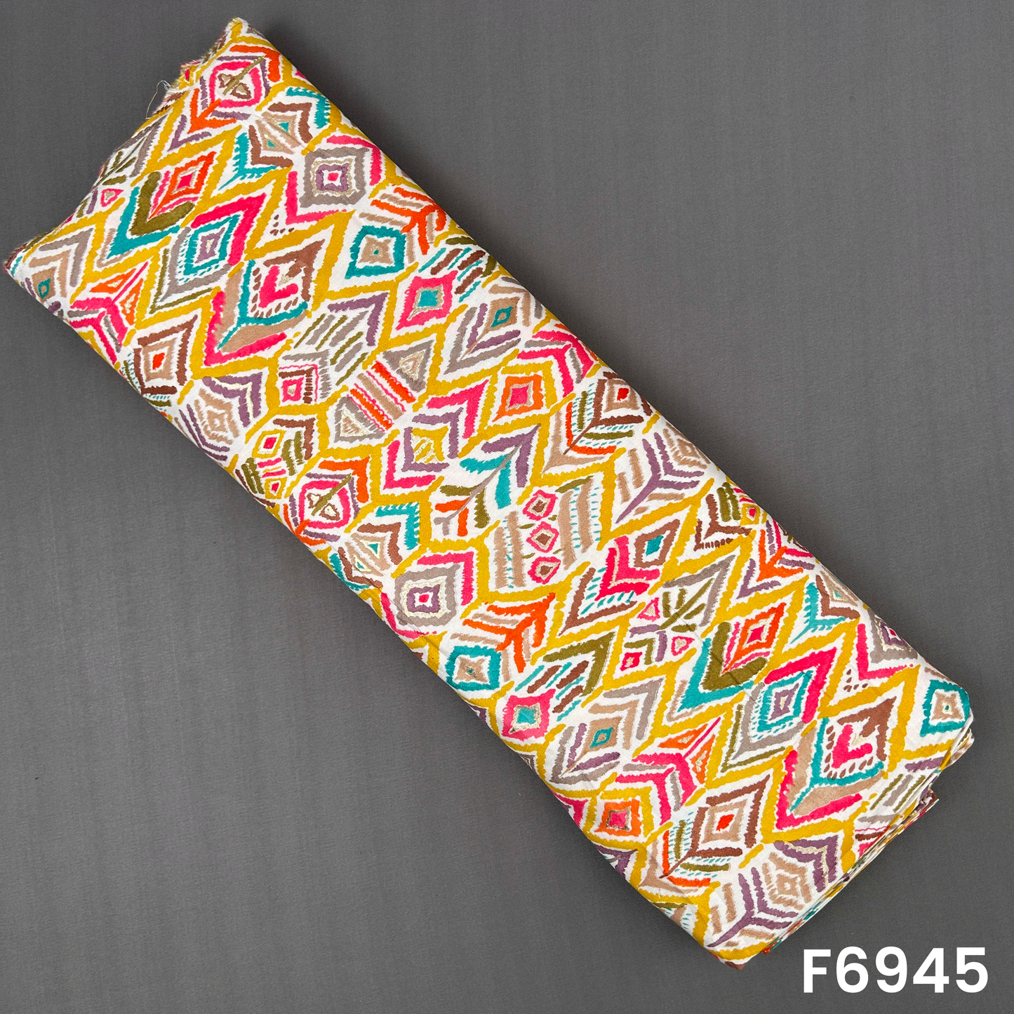 Folded rayon fabric F6945 displaying bright geometric diamonds in teal, yellow, pink, orange and olive tones